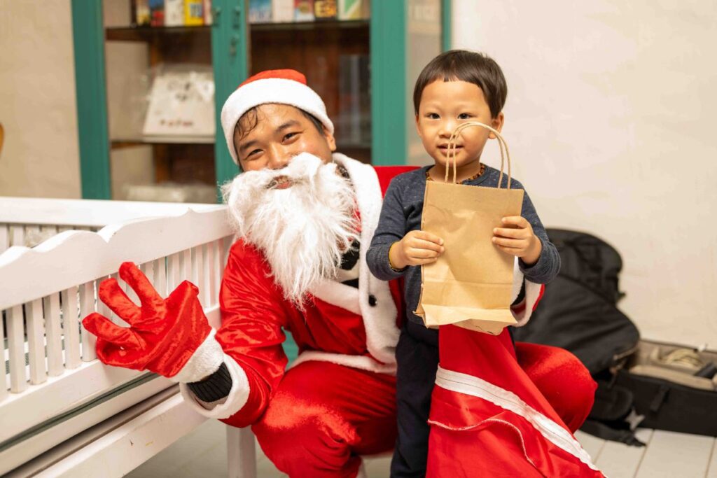 Santa Claus giving a gift to a smiling child during the Christmas Eve celebration at The DeckHouse, An Bang Beach, Hoi An.
