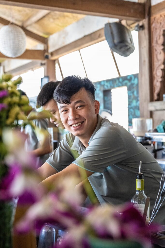 a happy team member of The DeckHouse An Bang Beach delivers drinks across the bar